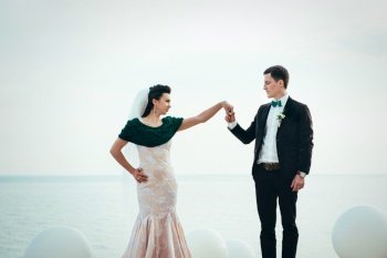 the groom in a brown suit and the bride in an ivory dress on the rocky seashore