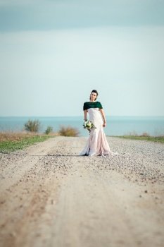 bride with a bouquet of flowers in an ivory dress and a knitted shawl on the road stretching into the distance