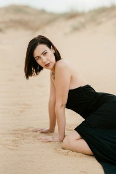girl in a black long dress in a sandy desert under a blue sky