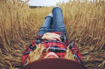 Young woman with country style is resting in a field of wheat 