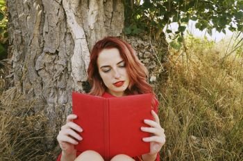 Young woman reading a red book in autumn          