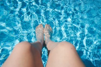 White woman legs against a turquoise pool water