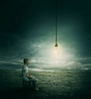 Creative idea concept with a man sitting on a chair in the middle of a desert, looking at a lightbulb