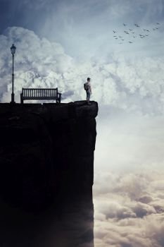 Inspirational imaginary view as a young boy with a bag in his back stand on the peak of a cliff above clouds, looking at the horizon, near a bench and a street lamp. Life journey opportunity concept.