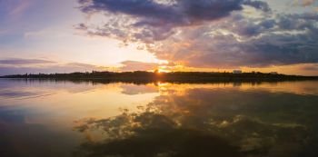 Wonderful sunset panorama over the city horizon with reflection on the calm lake water in a silent summer evening.