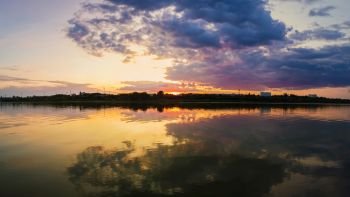 Wonderful sunset panorama over the city horizon with reflection on the calm lake water in a silent summer evening.