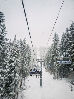 Wonderful winter scene with snow falling while climbing to the top of the mountain on a cable car gondola. Bukovel ski resort in Ukrainian Carpathians. Ski lift passing through the snowy fir forest