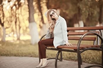 adult girl sitting on a bench in the park / beautiful model woman resting on a bench, cheerful happy girl
