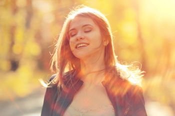 Cheerful happy young adult girl in sunlight rays and wind hair