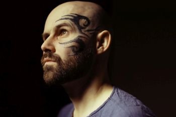 tattoo on the face,  male portrait in the form of an assassin, cosplay,  tattooed brutal man,  guy with a tattooed face