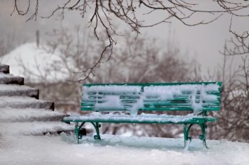 Winter Scene. Green Bench near the Stairs in the Park Covered with Snow. Wintertime Outdoors.