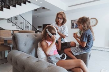 Photo of a three cheerful kids at home playing video games. Brothers shows sister how to play in virtual reality. Happy childhood.. Three Happy Kids Playing Video Games