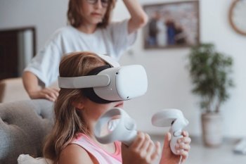The older brother teaches his little sister how to play a video game. Happy teenagers enjoying virtual reality. Fun weekend at home.. Happy Kids Playing Virtual Reality Game