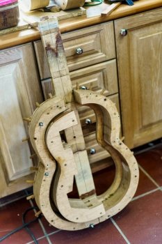 From above wooden mould for making Spanish flamenco guitar placed on tiled wall near cabinets in professional luthier workshop.. Wooden mould for making Spanish flamenco guitar in luthier workshop.