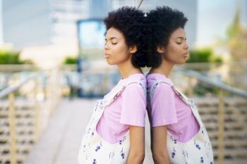 Side view of African American female with closed eyes standing near glass building on street of city against blurred background. Calm black woman near glass house