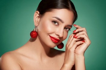 Portrait of beautiful young woman on green background, red lipstick and festive makeup, Christmas toy earrings, shiny glowing skin, Winter holidays concept