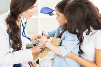 Young smiling female doctor and her little patient with teddy bear. Fmale doctor and little patient