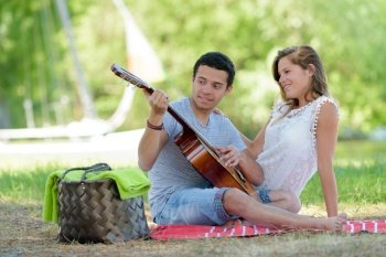beautiful young couple with guitar sitting on grass in park
