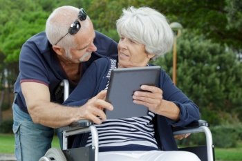woman in wheelchair with husband holding tablet in the park