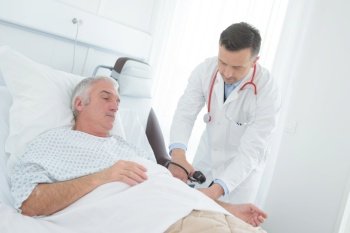 young male doctor checking blood pressure of senior male patient