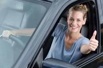 young woman in car shows thumbs up