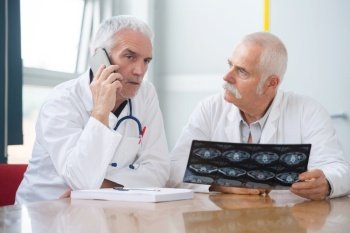 Two senior consultants holding xray, one talking on telephone