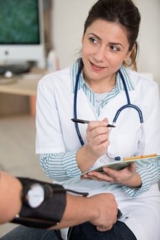 female doctor writing on clipboard while checking blood pressure