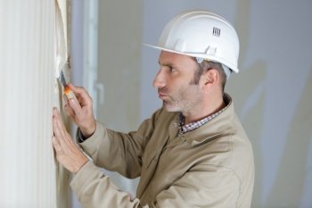 mature male builder stripping wallpaper with scraper