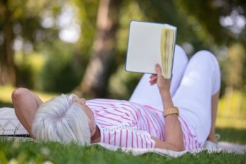 senior woman reading book laid on the grass