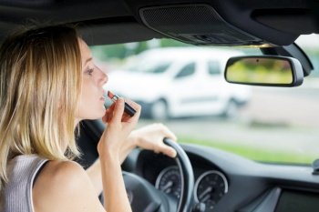 woman using a lip gloss and smiling while driving