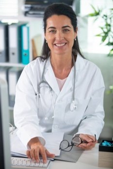 confident female doctor sitting at office desk and smiling