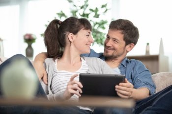 couple snuggled on the sofa looking at a tablet