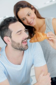 Woman offering man a bite of a croissant