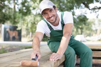 man worker in overalls painting bench in park