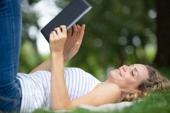 woman using tablet outdoor laying on grass