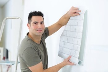 man unrolling roll of brick patterned wallpaper