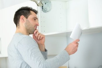 man fitting overhead kitchen cupboard reading instructions
