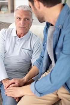 young compassionate man holding hand of unhappy elderly senior father