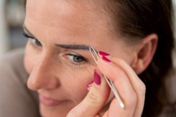 close up woman plucking her eyebrows with tweezers