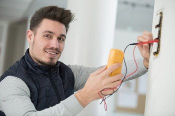 electrician checking the voltage level in wall socket cables