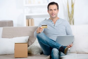 Portrait of man at home holding laptop and credit card