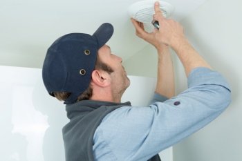 technician installing smoke detector on ceiling wall