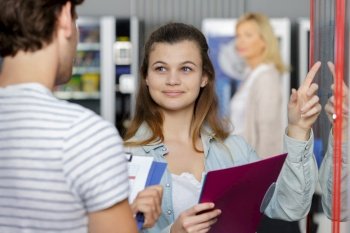 young woman asking friend what he wants from vending machine