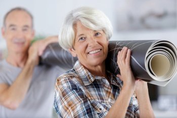 mature couple carrying carpet in new room