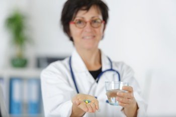 senior woman doctor offering pills and glass of water