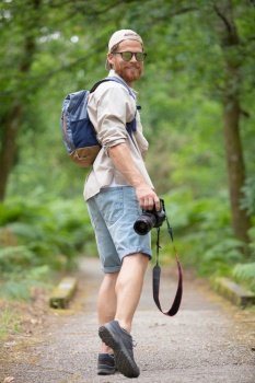 man wearing backpack walking in a forest holding dslr camera