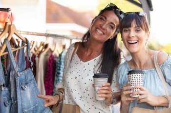 two happy women drinking coffee in outdoor clothes market