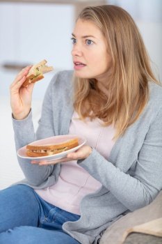 woman eating sandwich on sofa is shocked by television programme
