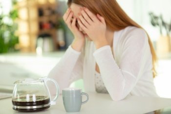 woman with a coffee holding her head in her hands