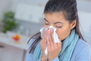 young woman blowing nose in bed ill with temperature